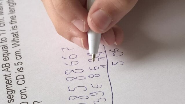 child, right-handed schoolchild hesitantly solves difficult task of adding numbers, 5th grade student writes down numbers in notebook with pen, math lessons, development of mathematical abilities