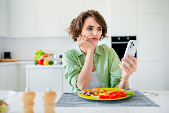 Photo of stressed bored lady dressed green shirt texting modern device eating dinner indoors house kitchen - Powered by Adobe