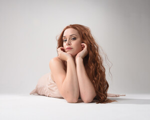 Full length portrait of beautiful brunette model  wearing a  pink dress. graceful sitting  pose, kneeling on floor gestural hands. shot from low angle perspective,  isolated on white studio background