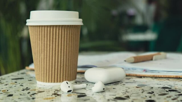 Zoom in out Take away coffee in craft recycling paper cup with paper notebook with wireless headphones. Mockup Coffee break. Audio healing, sound therapy wellness rituals, positive mental health