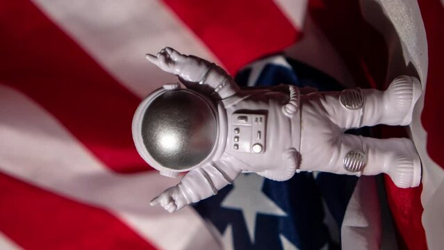 Vertical Zoom in out Plastic toy figure astronaut on American flag background Copy space. 50th Anniversary of USA Landing on The Moon Concept of out of earth travel, private spaceman commercial