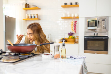 Fototapeta na wymiar Asian woman cooking healthy food fried pasta in cooking pan on modern kitchen island stove at home. Attractive girl preparing food for dinner party celebration meeting with friend on holiday vacation.