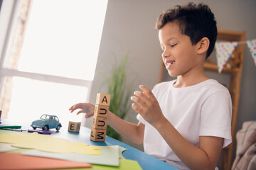 Photo of smiling charming small boy wear white t-shirt sitting table making cubes tower indoors...