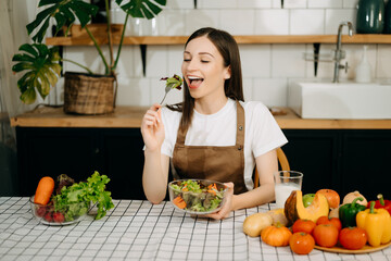 cheerful woman holding bowl with fresh mixed salad in home