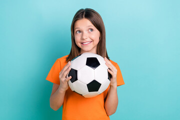Photo of cheerful satisfied little girl wear orange stylish t-shirt arms hold ball look empty space...