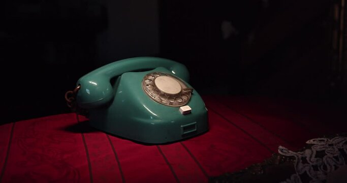The camera is slowly moving away from the dial phone placed on the table in the retro interior. The dramatic atmosphere of an unknown call