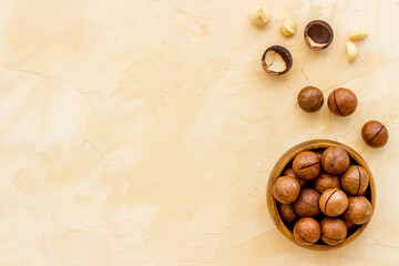 Wooden bowl of raw macadamia nuts in shell. Healthy protein snack background