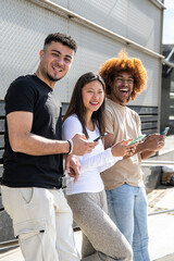 Three young diverse people laughing using smartphone and looking at camera. Multiracial group having fun and using phones standing in the street