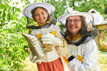 Happy female beekeeper with girl holding smoker