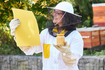 Female beekeeper offering honey jar and beeswax sheets