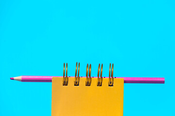 Notepad and pencil placed on blue backdrop in light