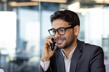 Young successful arab businessman boss talking on phone close up, man smiling contentedly inside...