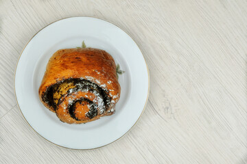 Bun with poppy seeds on a tin plate isolated on a wood background. Sweet homemade bun.