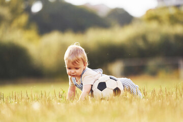 Cute little boy is on the field with soccer ball, at daytime