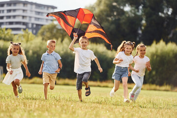 Running together. Group of kids are running and playing with kite on green field