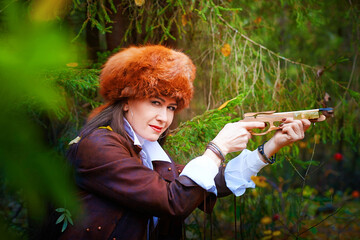 Girl in a leather jacket, a big red fox fur hat and with a crossbow in the forest in autumn. A...