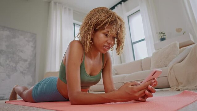 woman dressed activewear doing plank on the yoga mat holding smartphone watching exercises online class app
