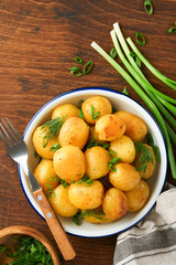 Naklejka na ściany i meble Boiled new or young potatoes with butter, fresh dill and onions in white bowl on dark old rustic wooden background. Tasty new boiled potatoes. Top view.