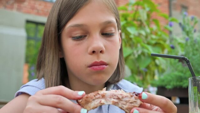 Little girl eating pork ribs in restaurant. 4k video footage in slow motion