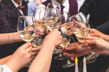 Group of guests celebrate and raise glasses, cheering with alcohol glasses with wine and champagne in the restaurant on corporate christmas birthday party event or wedding celebration
