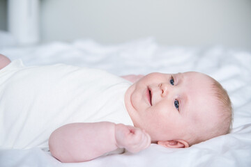 healthy smiling baby lies on his back on bed on white bedding