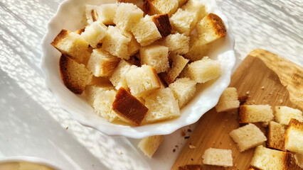 Homemade slices of diced dry white rye bread on cutting board and white plate. Crackers for food, healthy eating on table in sunny day, top view