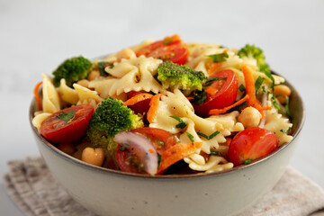 Yummy Homemade Vegan Pasta Salad with Tomato, Onion, Carrot, Broccoli, Chickpeas and Parsley in a Bowl, side view.