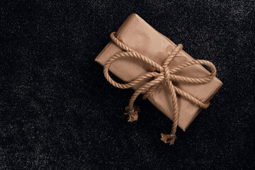 A present for a beloved man wrapped in paper, tied with a rope on a black table, close-up.