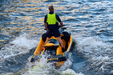 A standing man floats on an orange jet ski on the sea, close-up. The athlete floats on the water on an aquatic motorcycle.