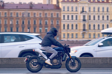 A man on a blue road motorcycle rides around the city after a rain. A motorcyclist in a black helmet rides a classic motorcycle on wet asphalt.