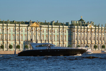 A black speedboat floats along the river, next to the embankment of a European city. Rent of boats and motor yachts.