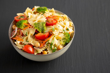 Yummy Homemade Vegan Pasta Salad with Tomato, Onion, Carrot, Broccoli, Chickpeas and Parsley in a Bowl, side view.