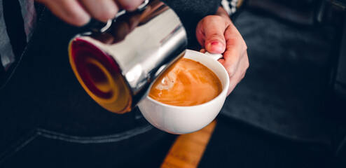 Close-up of the hand of a professional barista in a coffee shop making  pouring steamed milk into the coffee cup making latte menu