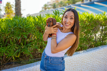 Young woman holds a dachshund in her hands outdoors