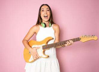Young female musician with a electric guitar isolated on pink background