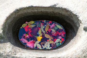 Japanese flower stone basin with floating pink flowers on water in zen spa at night in Kyoto street