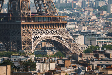 Fototapeta premium Daytime shot of the bronze Eiffel Tower in Paris, France under a hazy blue sky with city landscape.