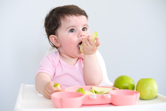 baby eating apple sitting in a high chair. weaning
