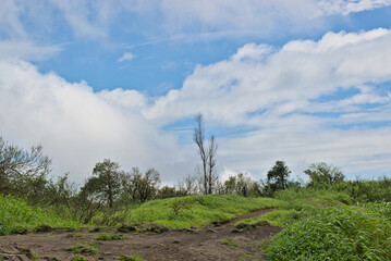 Panoramic landscape view of beautiful lush green scenery of Sinhagad fort with bright blue sky and huge white clouds in Pune, Maharashtra, India