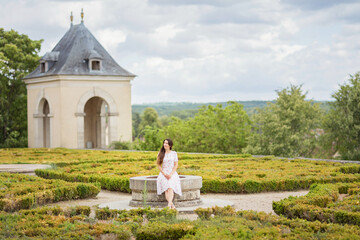 Portrait of attractive woman sitting in picturesque old park of small town near an ancient French castle