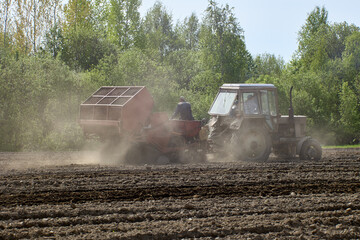 Potato planter works in farmers field as tractor trailer.