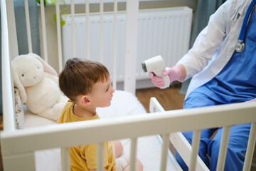 The nurse is checking the toddler's temperature with a contactless thermometer at home. Kid aged...