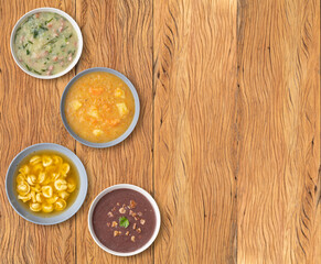 Various soup flavors in bowls over wooden table with copy space