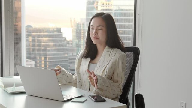 Young Asian business woman communicating by video conference call meeting. Female executive leader or hr manager talking having remote job interview working on laptop in modern office.