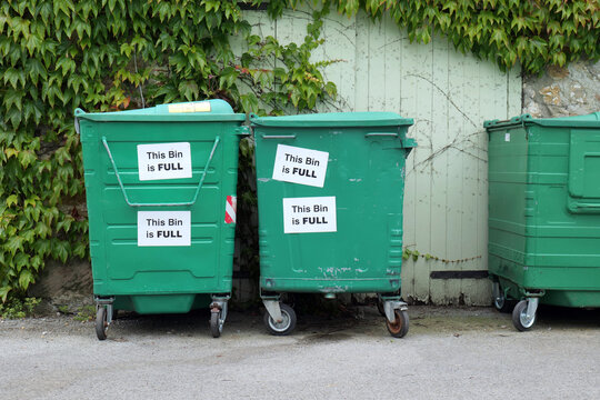 Metal garbage bins waiting to be collected, with signs stuck on them saying that they are full.