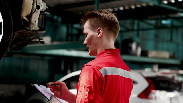 Caucasian mechanic man wearing red uniform inspect car reparing before sending to clients, lifestyle professional maintenance garage service concept, technician examine damage auto for insurance claim