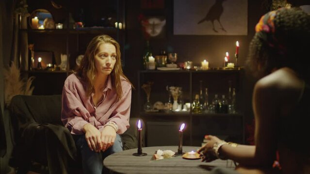 Female client talking to fortune teller while sitting in her room at prediction fate session