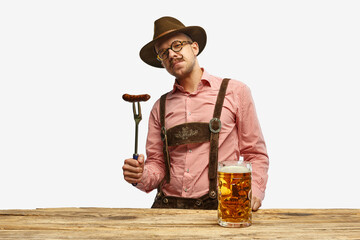 Bavarian mustache man in hat wearing traditional fest outfit holding hot fried sausage and looking...