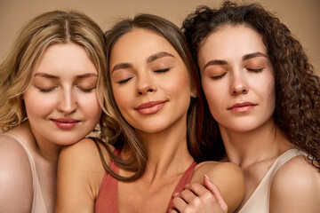 Close-up portrait of three young different women posing with closed eyes showing calmness, confidence and beauty. Healthy glowing skin, natural modern makeup.