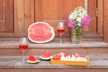Half of watermelon, pieces  of watermelon and melon, rose wine and hydrangea and astilbe flowers on steps of rustic wooden ladder.
